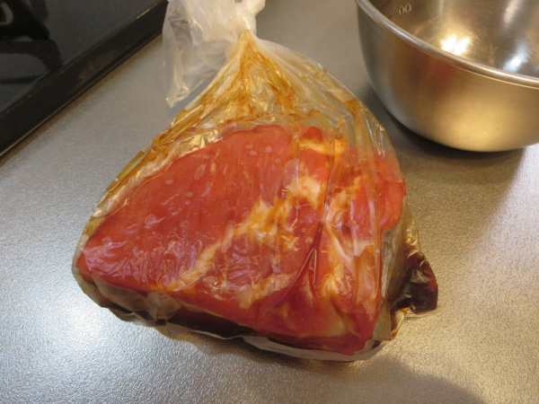 ポリ袋に入れた豚バラ肉を調味料で漬け込む