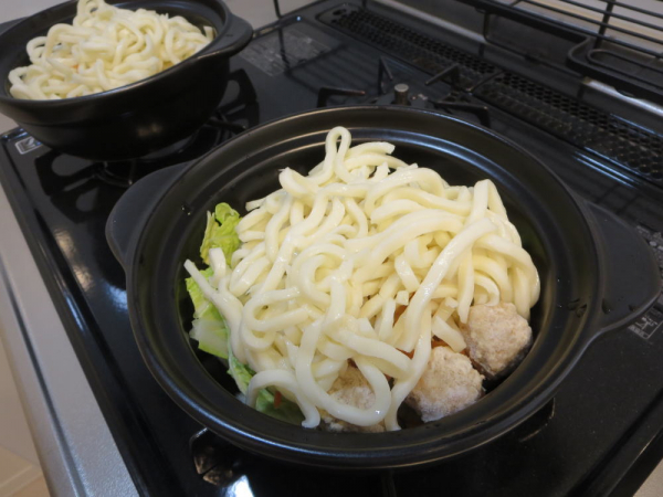 土鍋に野菜などを入れ、その上にうどん